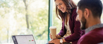 A woman holding a coffee cup while a man looking at laptop.