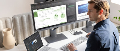 一位身穿蓝色衬衫的男士坐在桌前，使用显示有 Contoso CA 的计算机。