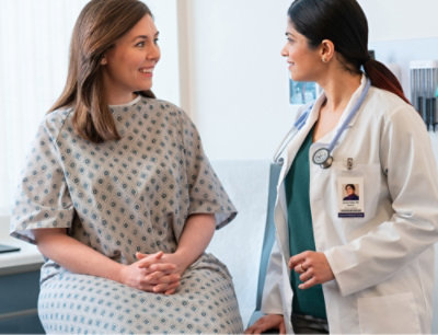 En lege som snakker med en kvinne i sykehuskjortel med langt hår.