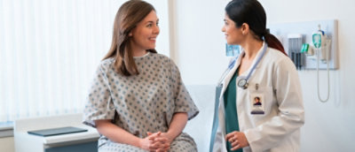 A woman in a hospital gown talking to a doctor.