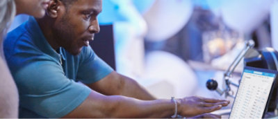 Un bărbat în cămașă albastră arată spre ecranul unui computer.