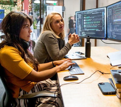 コンピューターの置かれているデスクに座っている人々のグループ。