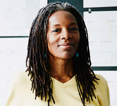 En person med dreadlocks och vit skjorta ler.