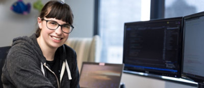 A woman wearing glasses smiling while sitting beside screen