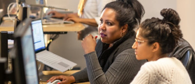 Two woman sitting at a desk with a laptop.