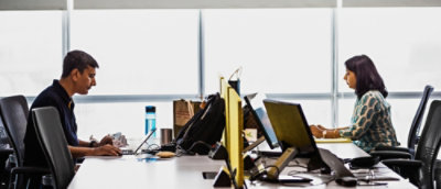 A desk with computers and a backpack.