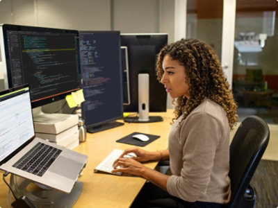 A person sitting at a desk working on a laptop placed on a stand.
