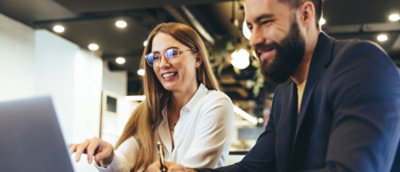 A woman and a man smiling while looking at a computer