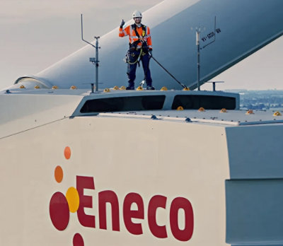 A person in an orange jacket and helmet stands on top of a large white building with a sign displaying the text ¿Eneco.