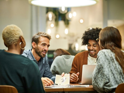 Sekelompok orang duduk mengelilingi meja dengan laptop terlihat.