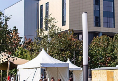 A group of people stands in front of a building with a white tent and pole nearby.