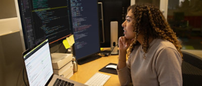 A person sitting at a desk looking at a computer screen with a stack of boxes nearby.