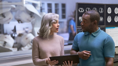 Two people standing in a room with various objects visible around them.