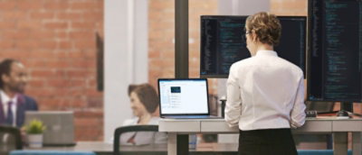A person in a white shirt standing in front of a laptop.