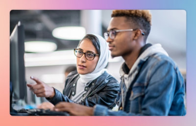 Two people are working at a computer; one is pointing at the screen while the other is focused on the display. 