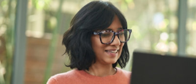 A woman wearing glasses looking at the screen and smiling