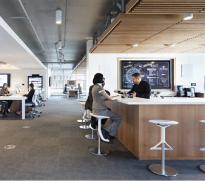 Modern office setting with people working at desks and two individuals conversing at a high-top counter.