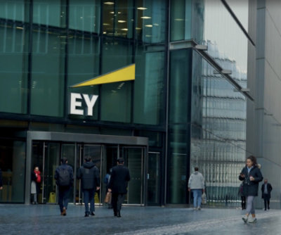 A group of people walking past a glass building with EY visible on its facade.