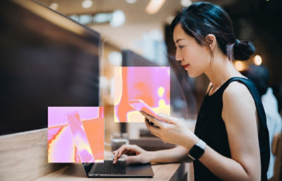 A women holding mobile and looking into laptop.