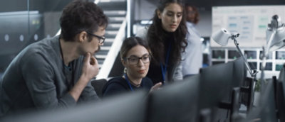 Three presons sitting together and looking into desktop screen.