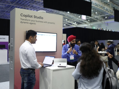 A group of people at a convention with text on a screen displaying Copilot Studio Transform your business with powerful, dynamic agents.