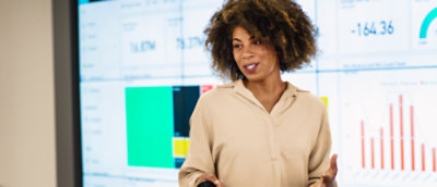 Une femme aux cheveux bouclés interagit avec un écran d’ordinateur, tendant la main vers celui-ci.