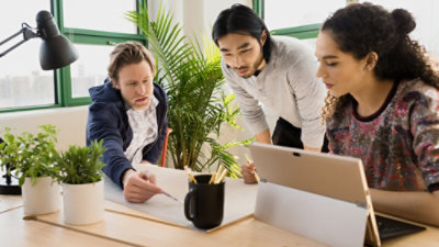 在现代化的办公室中，三个人围坐在笔记本电脑旁进行讨论。