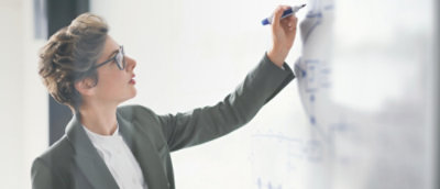 Person in a suit writing on a whiteboard with a blue marker