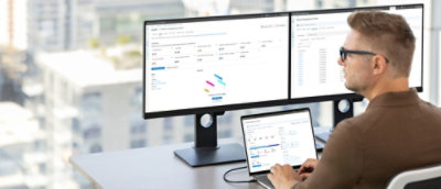 A person sitting at a desk using a laptop and a computer monitor.