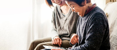A woman laughing while another woman looks at a tablet.