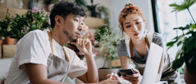 A man in a white shirt and apron looking at a phone with a woman.