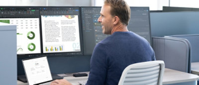 A man in a blue shirt sitting at a desk and looking at a computer screen.