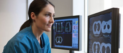 A woman in blue scrubs looking at a computer screen.