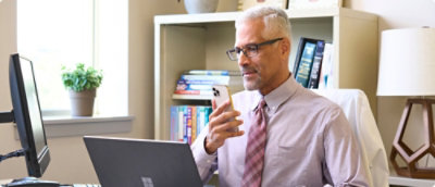 A person holding a phone and looking at a laptop.