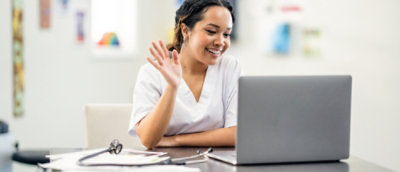 A woman waving at a laptop.