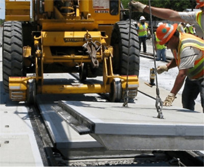 建築工人在戶外工地指揮黃色 Pettibone 起重機吊放混凝土板。