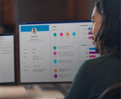 一人在光線昏暗的辦公室中操作多螢幕裝置，螢幕上顯示工作儀表板與個人資料詳情。