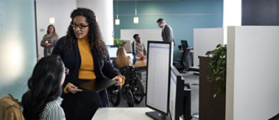 A person holding a folder in front of a computer screen.