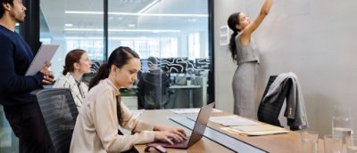 A person sitting at a desk typing on a laptop with a paper in hand.