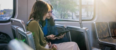 En gruppe personer, der sidder i en bus og kigger på en tablet.