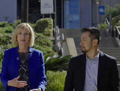 En mand i et jakkesæt og en kvinde i en blå jakke, der taler udenfor.