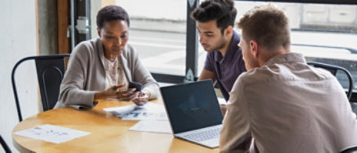 A group of people sitting around a table looking at a laptop.