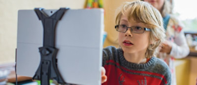 A young boy wearing glasses intently gazes at a tablet screen, focused on the content displayed.