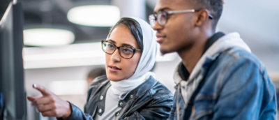 A man in a blue jacket and a woman wearing glasses and a scarf are looking at something.
