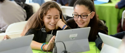 A close-up of a laptop with two people visible in the background.