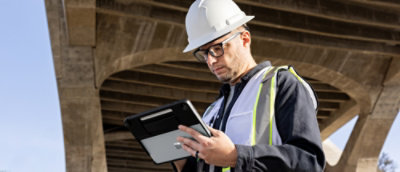 Een man met een veiligheidshelm en -vest die naar een tablet kijkt.