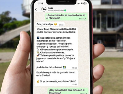 A hand holding a smartphone displaying a chat conversation in Spanish about activities at the Planetario Galileo Galilei.