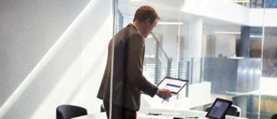 一位穿棕色穿棕色穿衣的人拿着一块白墙前的平板电脑。