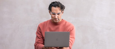 A man wearing glasses and a red shirt holding a laptop.
