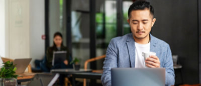 A person sitting at a table with a laptop and holding a cup.